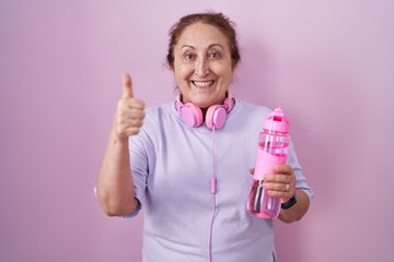 Senior woman wearing sportswear and headphones doing happy thumbs up gesture with hand. approving expression looking at the camera showing success.