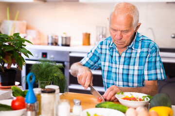 senor man preparing fresh vegetable salad at home in the kitchen