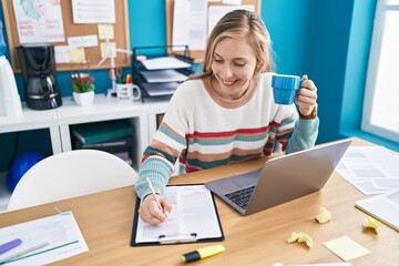 Young blonde woman business worker drinking coffee writing on document at office