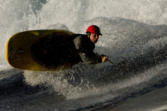 Male kayaker playboating and flipping in the air on a large wave in nice light.