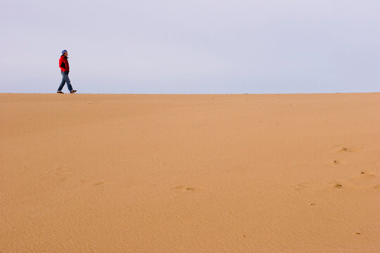 A young woman in her early thirties walks among the sand dunes, Florence, Oregon, United States.