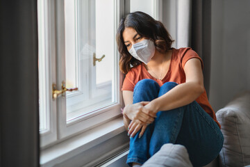 Depressed Young Arab Woman Wearing Protective Mask Sitting Near Windor At Home
