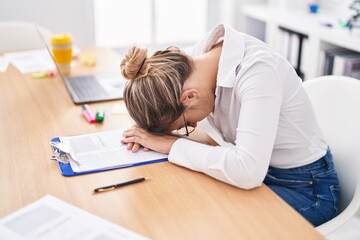 Young blonde woman business worker stressed with head on table at office