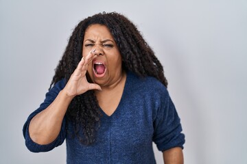 Plus size hispanic woman standing over white background shouting and screaming loud to side with hand on mouth. communication concept.