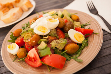 dish of fresh vegetables arugula, avocado, cherry tomatoes with olives and quail eggs on dining table
