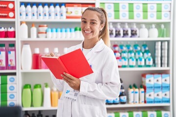 Young blonde woman working at pharmacy drugstore holding notebook celebrating crazy and amazed for success with open eyes screaming excited.