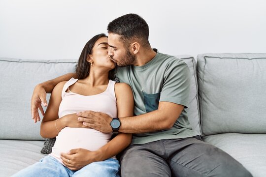 Latin man and woman couple hugging each other and kissing expecting baby at home