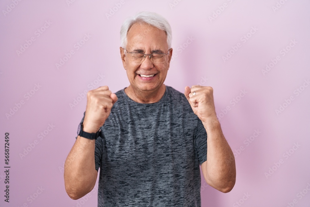 Poster Middle age man with grey hair standing over pink background excited for success with arms raised and eyes closed celebrating victory smiling. winner concept.