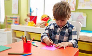Adorable hispanic boy preschool student sitting on table drawing on paper at kindergarten