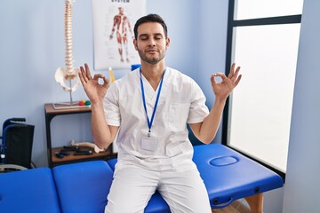 Young hispanic man with beard working at pain recovery clinic relax and smiling with eyes closed doing meditation gesture with fingers. yoga concept.