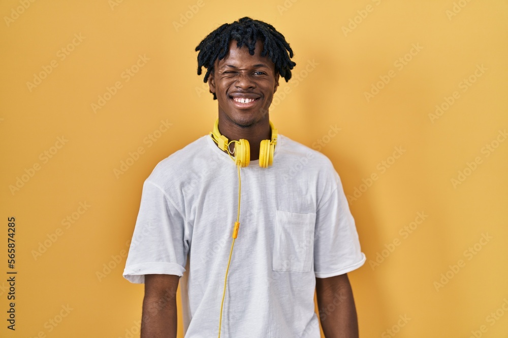 Sticker young african man with dreadlocks standing over yellow background winking looking at the camera with