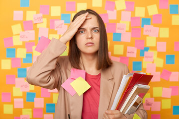 Portrait of serious shocked brown haired woman in jacket posing against colorful sticky notes on...