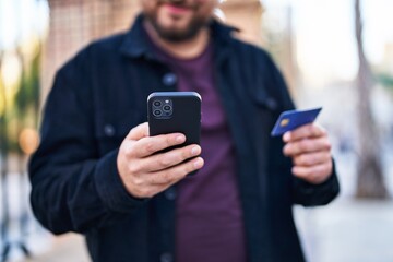 Young hispanic man using smartphone and credit card at street