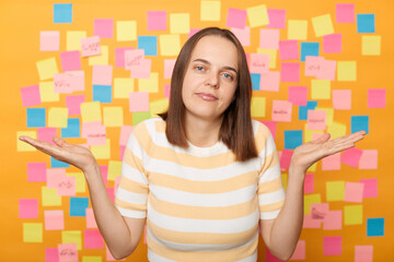 Horizontal shot of confused upset young adult woman wearing T-shirt posing against yellow paper...