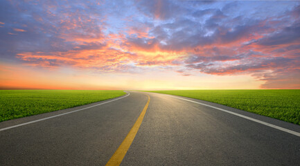 Tarmac road in slope grass field with sunset background.