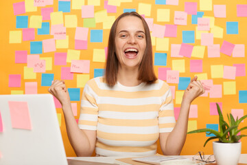 Horizontal shot of excited amazed happy young adult woman wearing T-shirt posing against yellow...