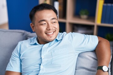 Young chinese man smiling confident sitting on sofa at home