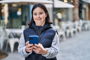 Young woman with down syndrome smiling confident using smartphone at street
