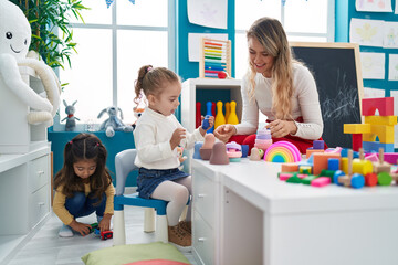 Teacher with girls playing with geometry blocks sitting on table at kindergarten
