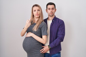 Young couple expecting a baby standing over white background showing middle finger, impolite and...