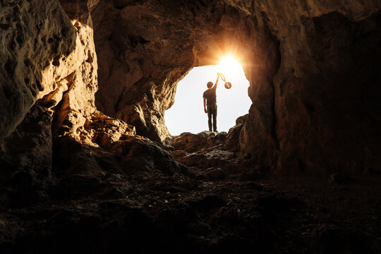 A silhouette of a young man stands at the mouth of a cave holding up a medal marked with the number one.
