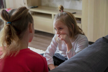 Obraz na płótnie Canvas Two schoolgirls sit on the sofa in the living room and discuss misunderstandings, difficulties and family problems. The concept of help and compassion within the family