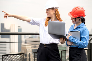 Female engineer and architect coworker standing outdoors on rooftop of construction site looking forward for apartment, housing development. Maintenance building contractor discussion with teamwork