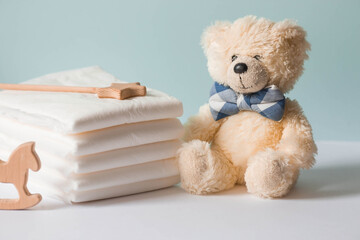 Wooden toys, a bear in a bow tie, a stack of disposable diapers and baby supplies on the changing table. Space for text.
