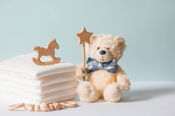 Wooden toys, a bear in a bow tie, a stack of disposable diapers and baby supplies on the changing table. Space for text.