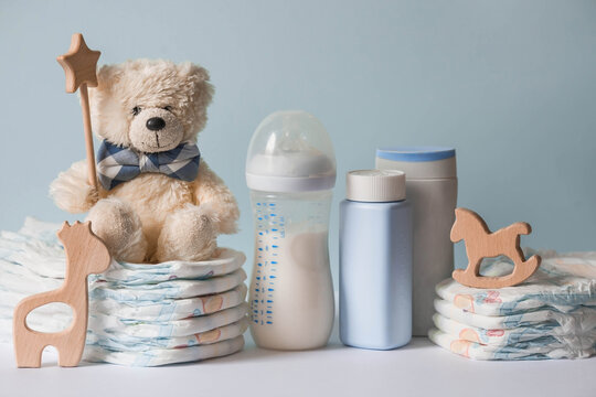 Wooden toys, a bear in a bow tie, a stack of diapers, bottles without labels and baby supplies on the changing table. Space for text.