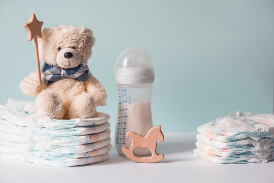 Wooden toys, a bear in a bow tie, a stack of diapers, a bottle and baby supplies on the changing table. Space for text.