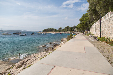 Beautifully paved seafront promenade with stone wall and pinewood connecting the harbor and resort town of Hvar, Croatia and offering great views to the Pakleni islands along the rocky coast