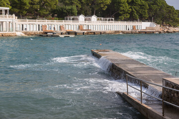 Stormy sea with splashing waves at a landing stage opposite to a beach club at Bonj beach on the island Hvar, Croatia