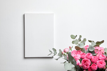 Blank canvas mockup hanging on white wall and pink flowers in interior. White canvas and floral decor