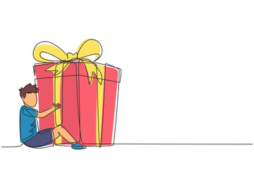 Continuous one line drawing happy little boy sitting and hugging huge gift box with ribbon bow wrapped in front of his in arms. Children accept birthday gift or present. Single line draw design vector