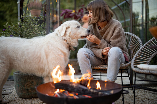 Young woman spends evening time with her cute white dog, sitting by the fire in garden at cozy and beautiful atmosphere