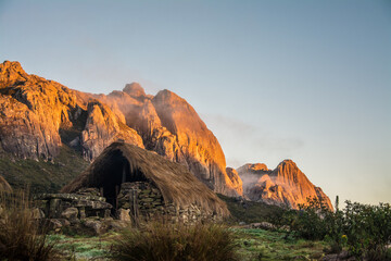 Andringitra National Park during the sunrise. Stone hut with tratched roof with rocky mountaind in the background with morning sun. Madagascar. 