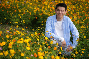 smile Chinese young man squat at yellow flowers filed, looking at camera