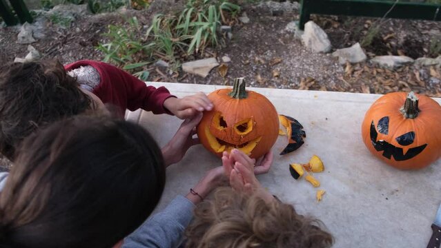 Preparing pumpkin for Halloween. Mother with children drawing out details of the face of the carved Halloween pumpkin. Emptying seeds inside pumpkin outlining the face eyes mouth with knife 