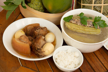 Family dinning table of Tet holiday or Lunar New Year with traditional foods: pork belly and eggs braised in coconut water, pickles, rice, Banh Tet (rice cake), fried vegetables, bitter melon soup