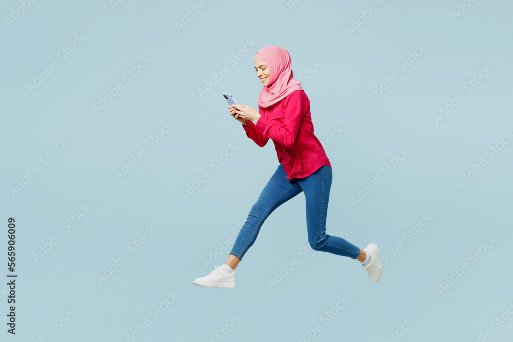 Wall mural full body side profile view young arabian asian muslim woman in pink abaya hijab jump high use mobil