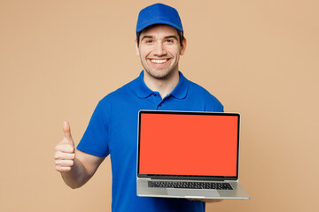 Delivery guy fun employee IT man wear blue cap t-shirt workwear work as dealer courier hold use work on blank screen workspace area laptop pc computer show thumb up isolated on plain beige background.