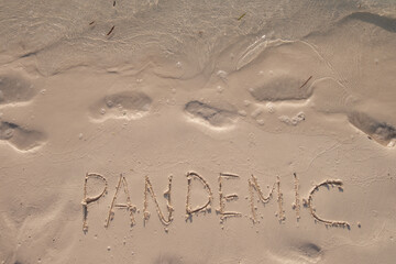 Pandemic. Handwritten text on smooth sand beach