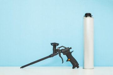 Black professional foam spray gun with gray container on white table at light blue wall background....