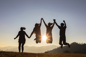 Silhouette group of happy young people jumping on mountain beautiful summer sunset