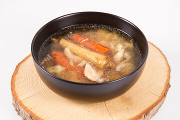 Chicken soup with noodle and carrot and parsley roots, chicken meat visible, in a bowl on a wooden pad