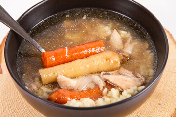 Chicken soup with noodle and carrot and parsley roots, chicken meat visible, in a bowl on a wooden pad