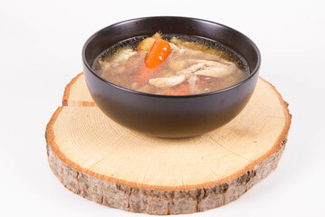 Chicken soup with noodle and carrot and parsley roots, chicken meat visible, in a bowl on a wooden pad