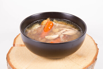 Chicken soup with noodle and carrot and parsley roots, chicken meat visible, in a bowl on a wooden pad
