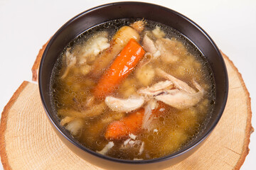 Chicken soup with noodle and carrot and parsley roots, chicken meat visible, in a bowl on a wooden pad